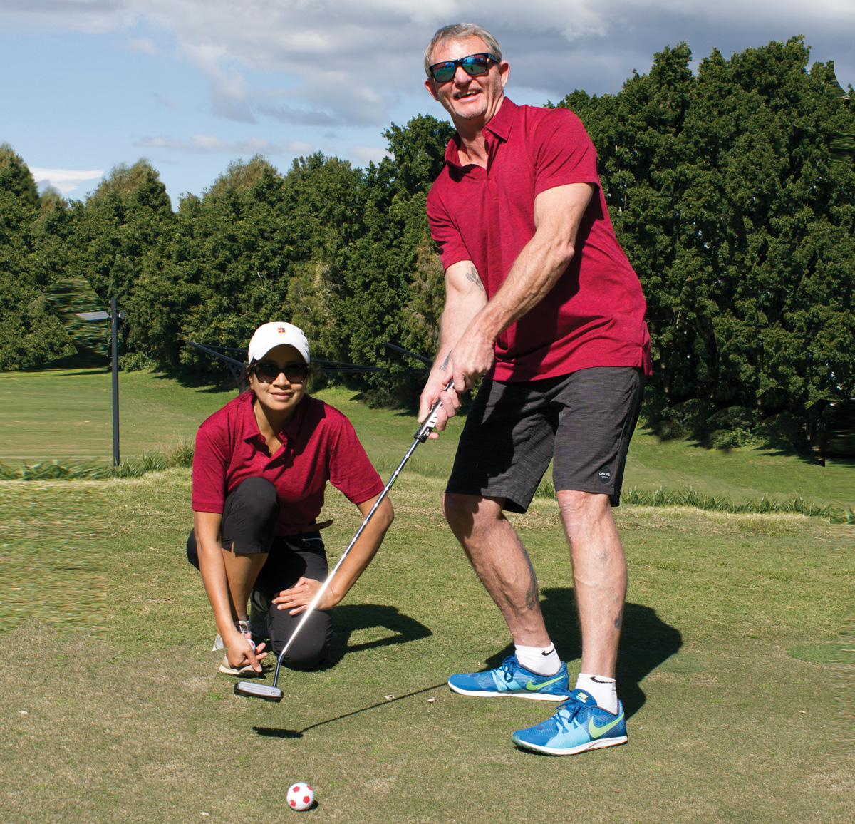 a blind golf caddy kneeling down behind a smiling and very handsome and fit blind golfer.